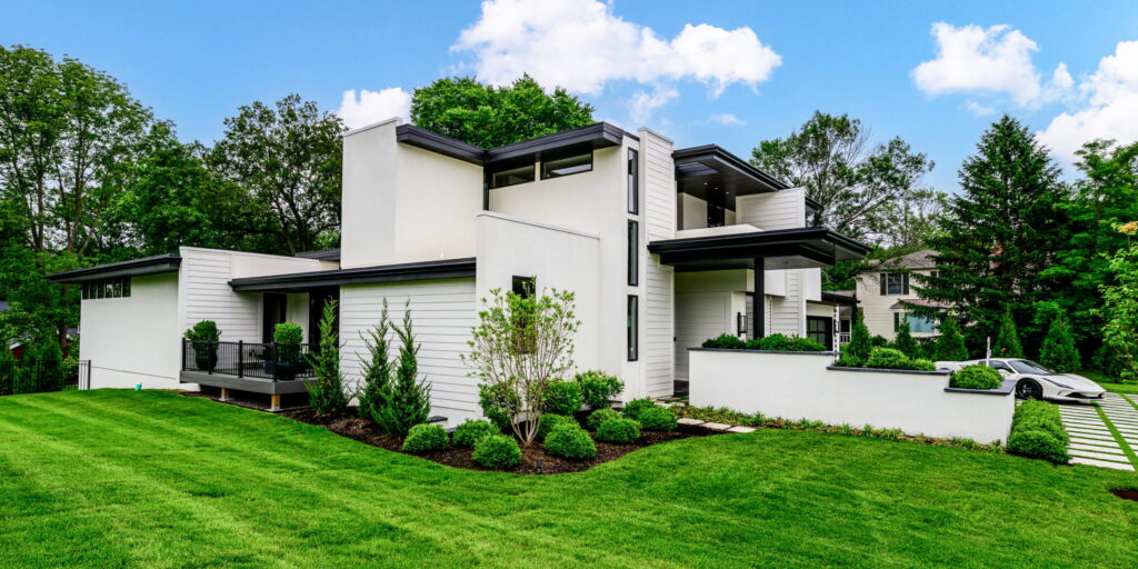 Modern white, flat-roofed house with a manicured green lawn under a bright blue sky.