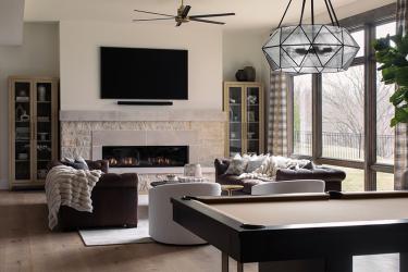 Spacious modern living room with a fireplace, wall TV, gray sectional sofas, and a pool table beside large windows.
