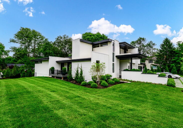 Modern white, flat-roofed house with a manicured green lawn under a bright blue sky.