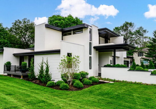 Modern white, flat-roofed house with a manicured green lawn under a bright blue sky.